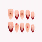 Scarlet Aristocrat: nude almond press-on nails with red French tips, red gems and gold accents, arranged on a pale background.