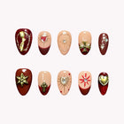 Magdalena’s Crimson Relic: burgundy and nude almond press-on nails with gold-tone hearts, stars and decorative motifs, set arranged on a pale background.