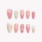 Evelina’s Porcelain Rose: pink and white almond press-on nails with delicate floral patterns and fine gold-tone outlines, set arranged on a pale background.