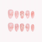 Flora’s Pastel Dream: pink almond press-on nails with white floral outlines and raised blossoms, arranged on a pale background.
