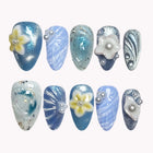 Mermaid Cove Bliss blue and teal almond nails with raised yellow and white flowers, shell ridges and pearly accents.