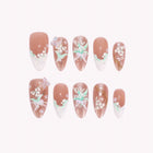 Muguet’s Gossamer Wing: nude almond press-on nails with white floral tips and iridescent butterfly decorations, arranged on a pale background.