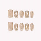 Gilded Mirage: nude square press-on nails with gold-toned frames and raised pearl-like accents, arranged on a pale background.