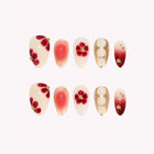 Garnet Camellia Muse: cream and red almond press-on nails with red flowers and gold-tone accents, set arranged on a pale background.