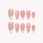 Persephone’s Spring Crown: pink almond press-on nails with white pointed tips, shell ridges and raised flowers, arranged on a pale background.