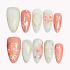 Antheia's Coral Wreath coral pink and milky white almond nails with raised flowers, gold-colored borders and bow details.