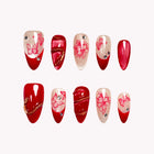 Eden’s Ruby Serpent: red and nude almond press-on nails with floral line art and gold-tone curved details, set arranged on a pale background.