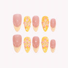 Nymph’s Amber Garden: nude and yellow almond press-on nails with pointed French tips and raised flowers, arranged on a pale background.