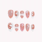 Psyche’s Pearl Whisper: pink press-on nails with white petal motifs, iridescent accents and pearl-like beads, arranged on a pale background.