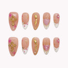 Sacred Heart Serenade nude pink almond nails with gold-colored crosses, tiny pink flowers and pale decorative tips.