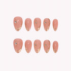 Eos’ Golden Whisper: peach-pink almond press-on nails with fine gold-toned tips and tiny gems, arranged on a pale background.