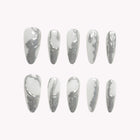 Metropolis Liquid Silver: long silver-tone almond press-on nails with irregular reflective metallic patches, set arranged on a pale background.