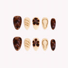 Amber Tortoise Nouveau: brown tortoiseshell and cream almond press-on nails with dark flowers and gold-tone raised outlines, set arranged on a pale background.