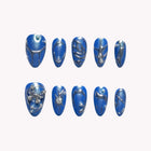 Cosmic Morpho Chrome: blue almond press-on nails with silver-tone swirls and raised metallic decorations, set arranged on a pale background.