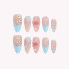 Fae’s Azure Whisper: pink almond press-on nails with blue tips, raised flowers and small bead accents, set arranged on a pale background.