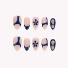 Cobalt Dynasty: nude and navy press-on nails with blue flowers, curved tips and gold accents, arranged on a pale background.