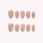 Selene's Golden Veil: nude almond press-on nails with gold-toned edging, crescent moons and tiny gems, arranged on a pale background.