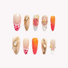 Ambrosia's Coral Voyage: long almond press-on nails with orange gradients, red-dotted tips and raised gold-tone accents, set arranged on a pale background.