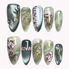 Forest Ember Spell green almond nails with dark red branch patterns, gold-colored swirls and reflective accents.
