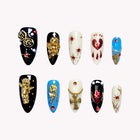 Cherubim's Gilded Vow: black, white and blue almond press-on nails with ornate gold-tone motifs and red accents, set arranged on a pale background.