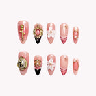 Rosaline’s Gilded Cameo: pink almond press-on nails with white flowers, gold-tone cameos and a black accent tip, set arranged on a pale background.
