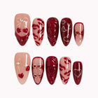 Aphrodite’s Stolen Kiss red and pink long almond press-on nails with lip art, bows, and hearts on a white background.