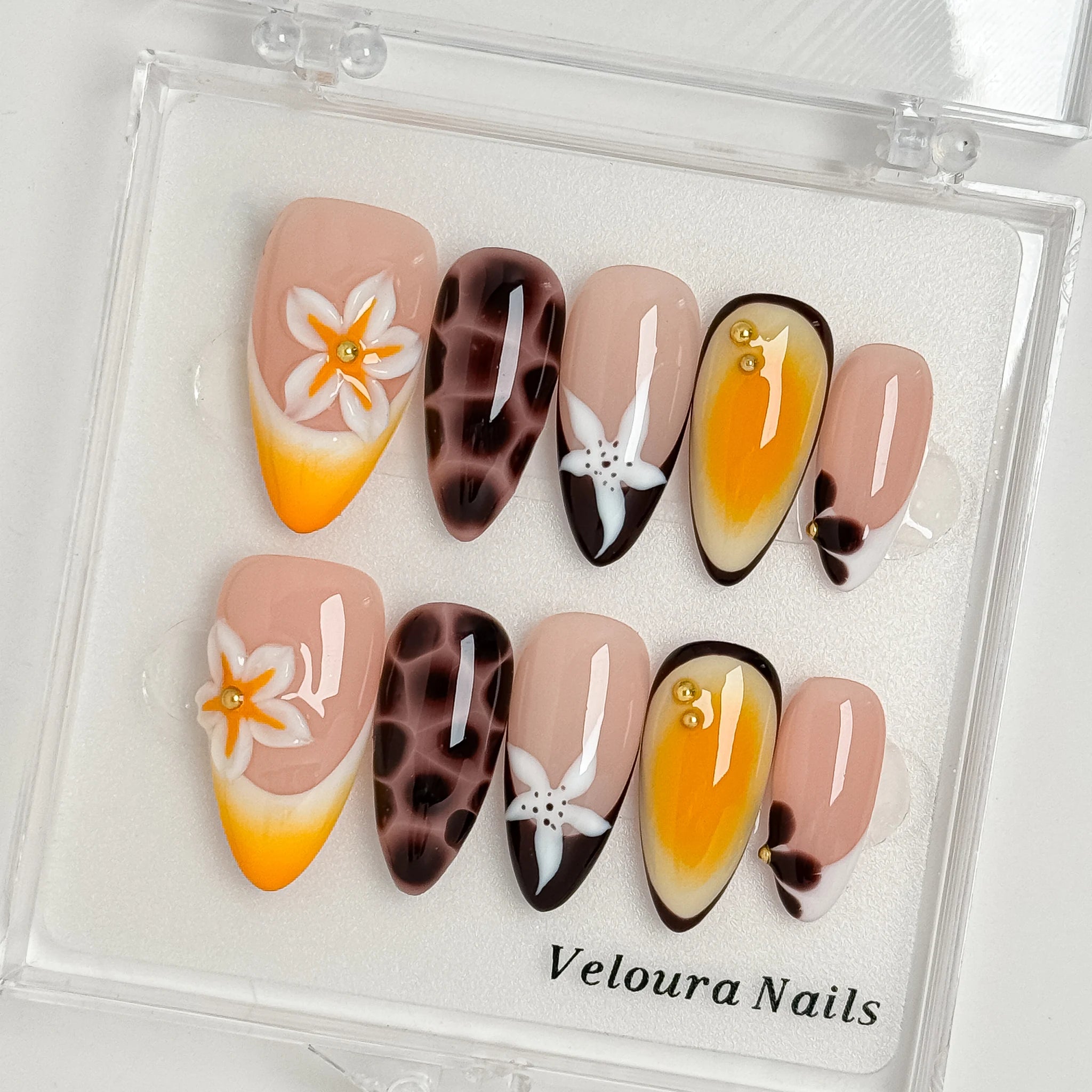 Vintage Havana Bloom: yellow, nude and brown almond press-on nails with spotted patterns, white flowers and starfish accents, displayed in a clear Veloura Nails case.