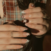 Burgundy Bow Sonata: hands against plaid fabric showing burgundy and nude nails with white bows and patterned French tips