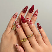 Aphrodite’s Stolen Kiss red and pink press-on nails worn on two hands with gold rings.