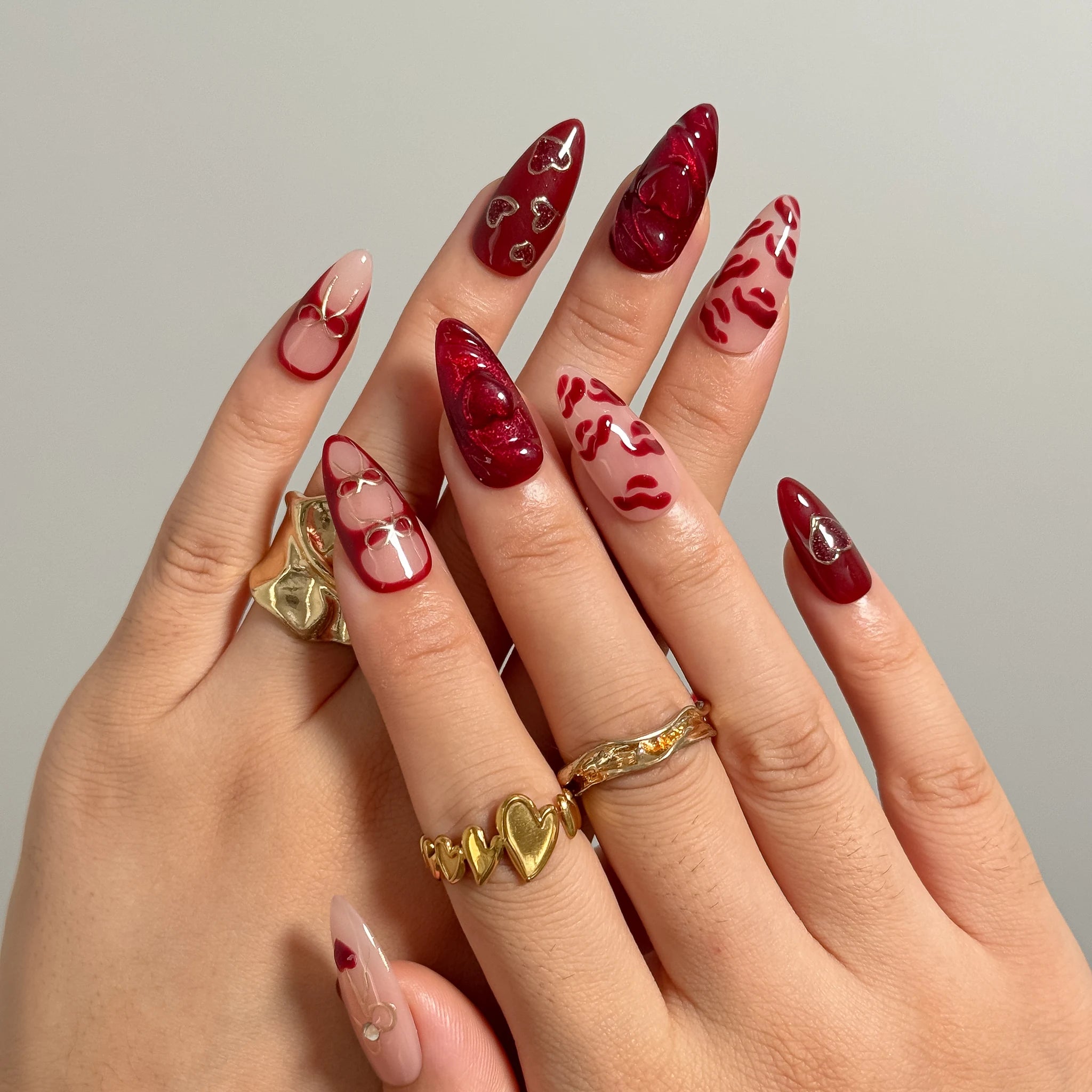 Aphrodite’s Stolen Kiss red and pink press-on nails worn on two hands with gold rings.