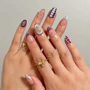 Chimera’s Amber Mosaic burgundy and nude press-on nails worn on two hands with gold rings.