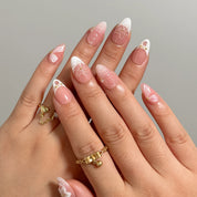 Galatea’s Ivory Bloom pink and white floral press-on nails worn on two hands with gold rings.
