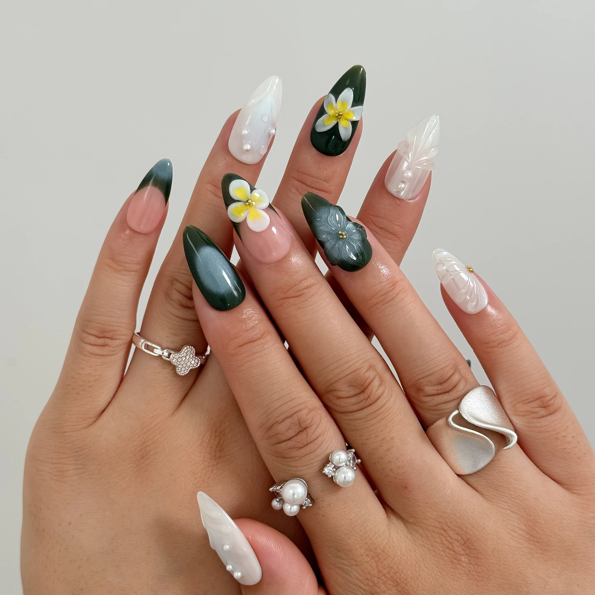 Overlapping hands wearing deep green nails with raised white-and-yellow flowers and milky white accents.