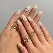 Nereid's Radiance yellow and nude press-on nails worn on two hands with pearl and gold rings.