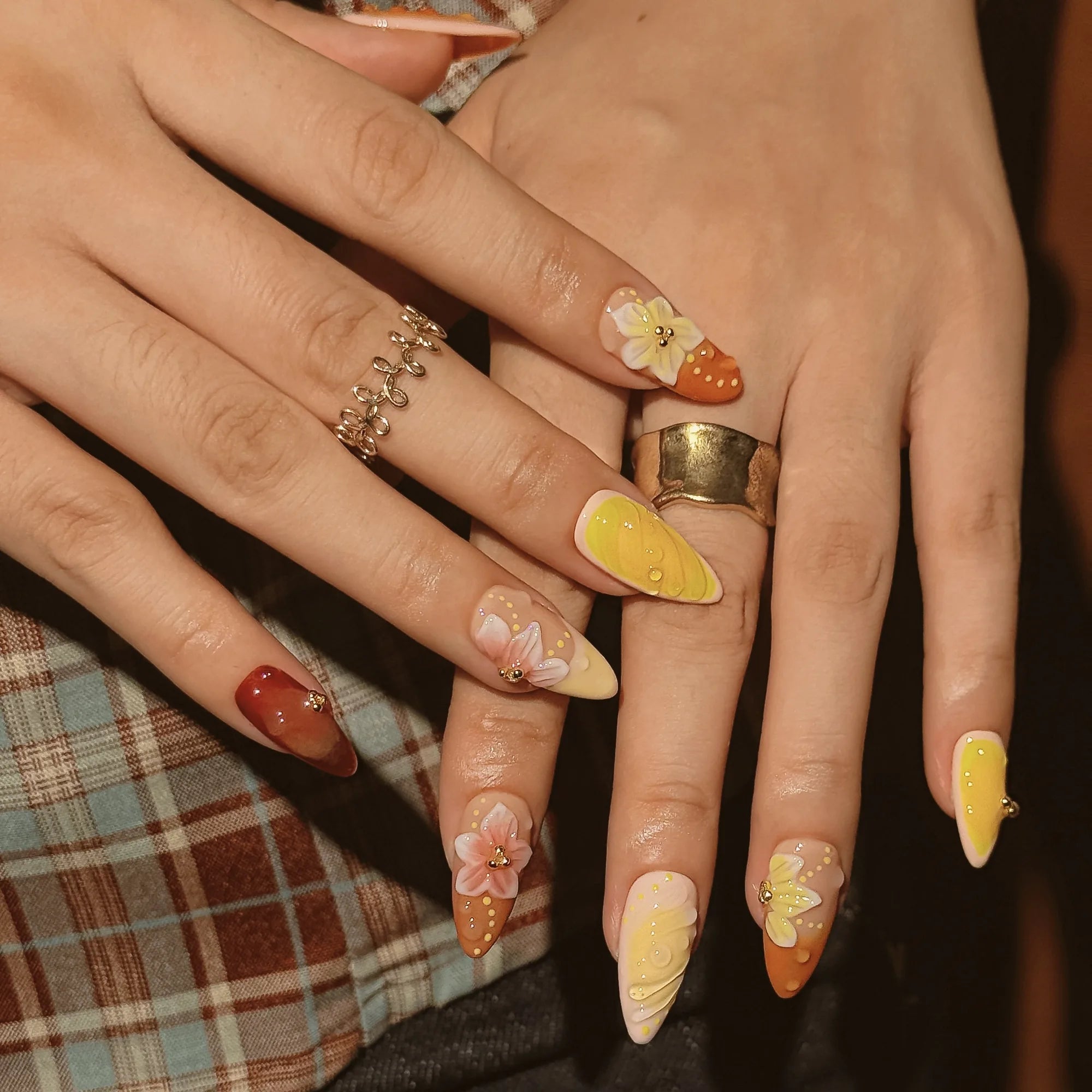 Harvest Citrus Bloom: overlapping hands against plaid fabric showing warm-colored nails with sculpted flowers and ridges