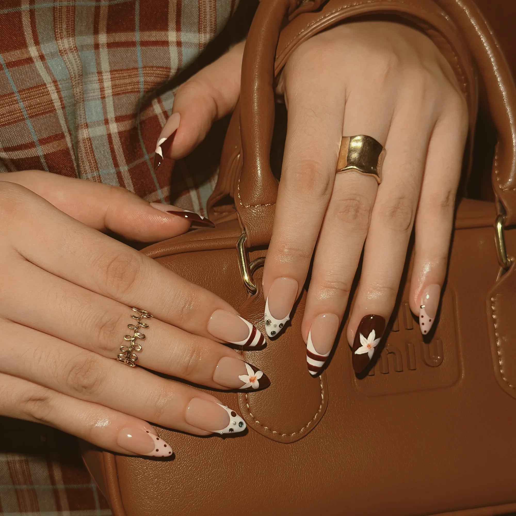 Burgundy Bow Sonata: hands on a brown handbag showing white bow accents and burgundy-striped nail tips