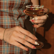 Crimson Garden Jewel: hands holding a stemmed glass, showing burgundy-tipped nails with floral and jeweled accents