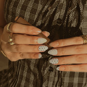 Porcelain Dot Muse: hands against plaid fabric showing white dotted nails, textured white panels and glossy nude accents