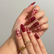 Close-up of Aphrodite’s Stolen Kiss long almond nails with red lips, bows, and heart details.
