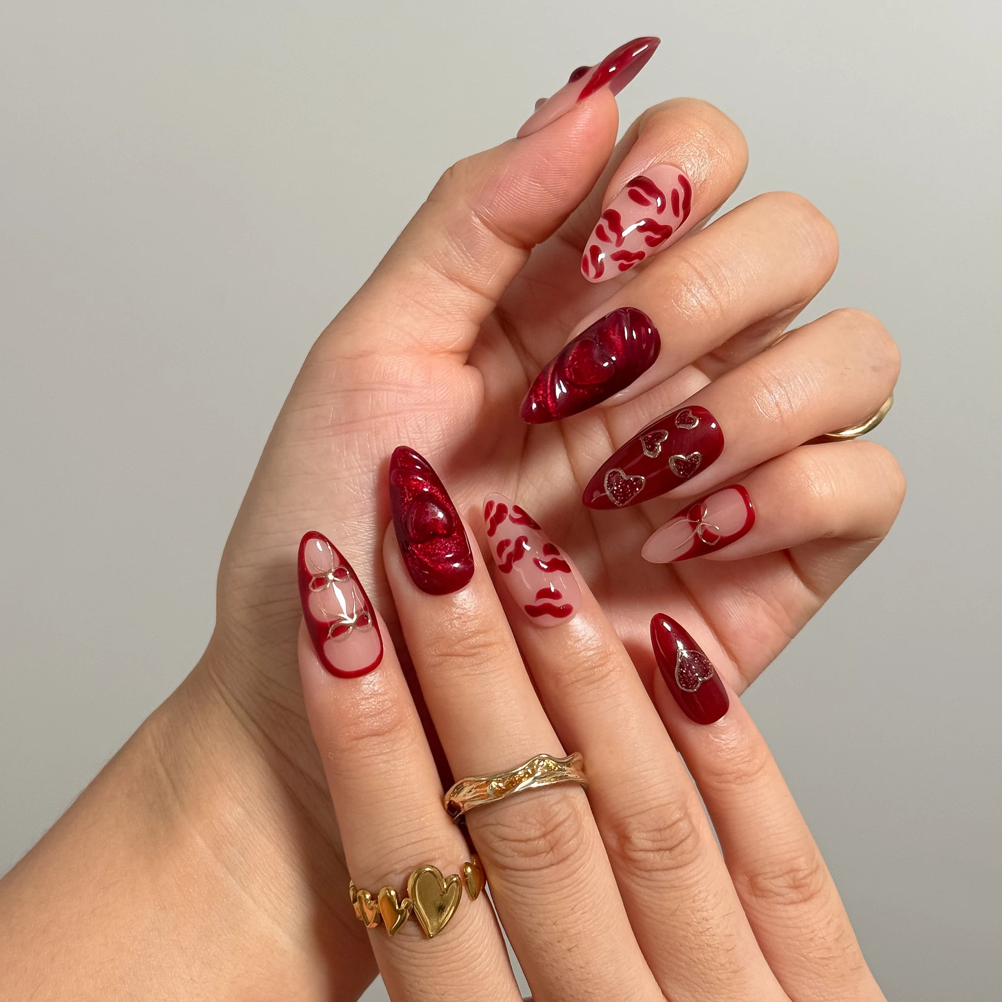 Close-up of Aphrodite’s Stolen Kiss long almond nails with red lips, bows, and heart details.