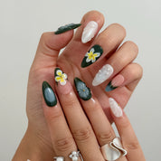 Curled and resting hand poses showing green floral nails, pale textured accents and dark green tips.