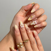 Close-up of Nereid's Radiance long almond nails with raised white flowers, shells, and yellow tips.