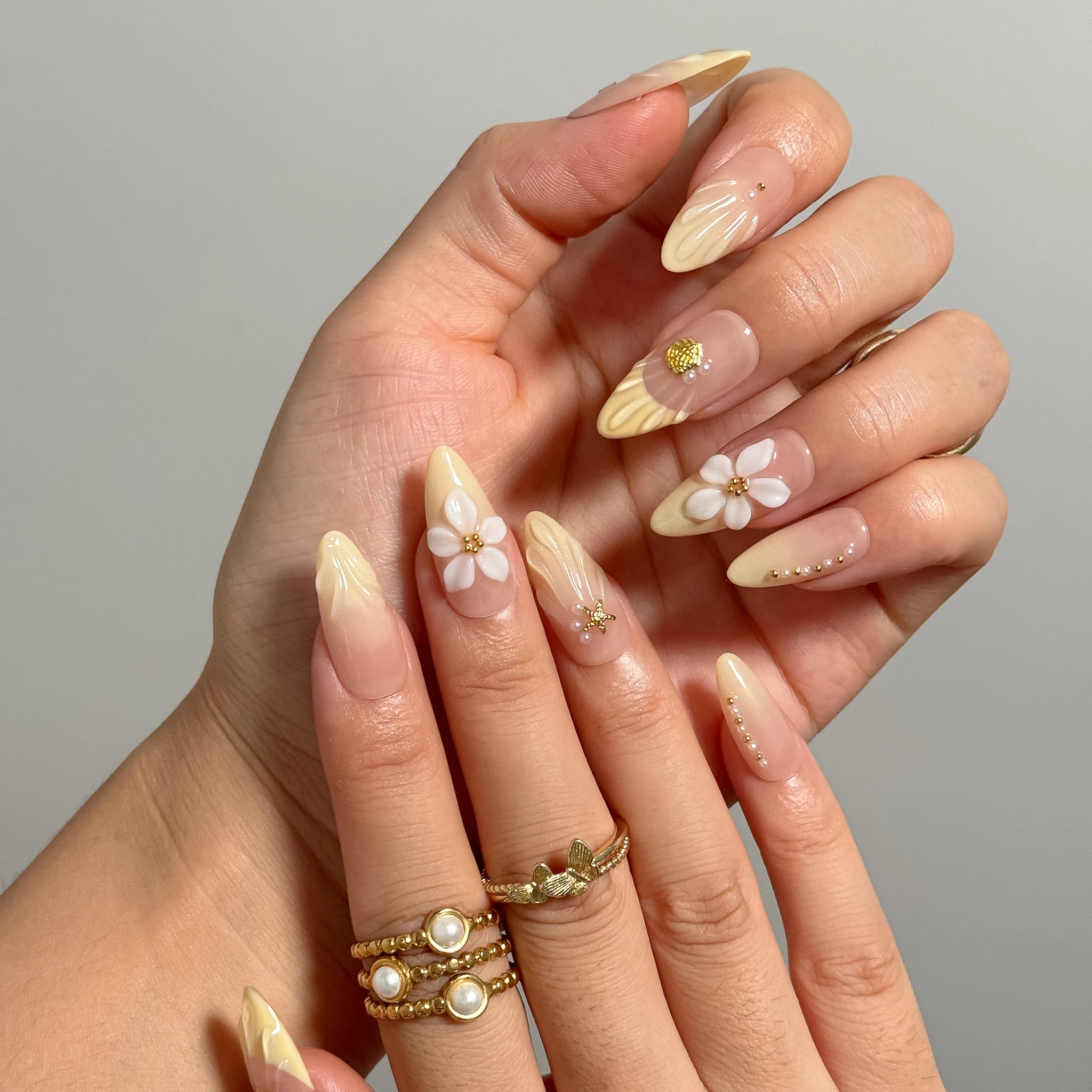 Close-up of Nereid's Radiance long almond nails with raised white flowers, shells, and yellow tips.