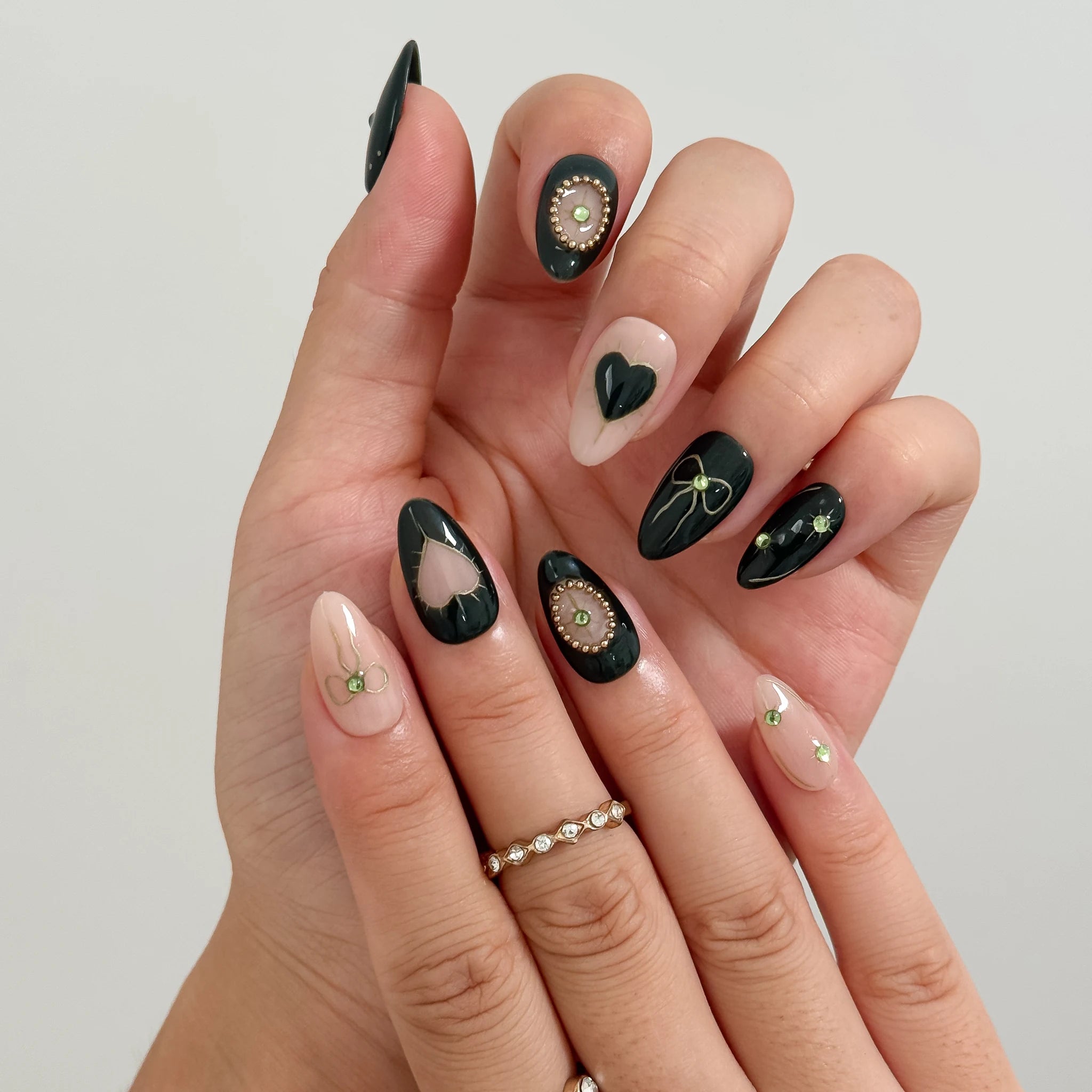 Curled and resting hand poses showing black and nude almond nails with gold-colored detailing.