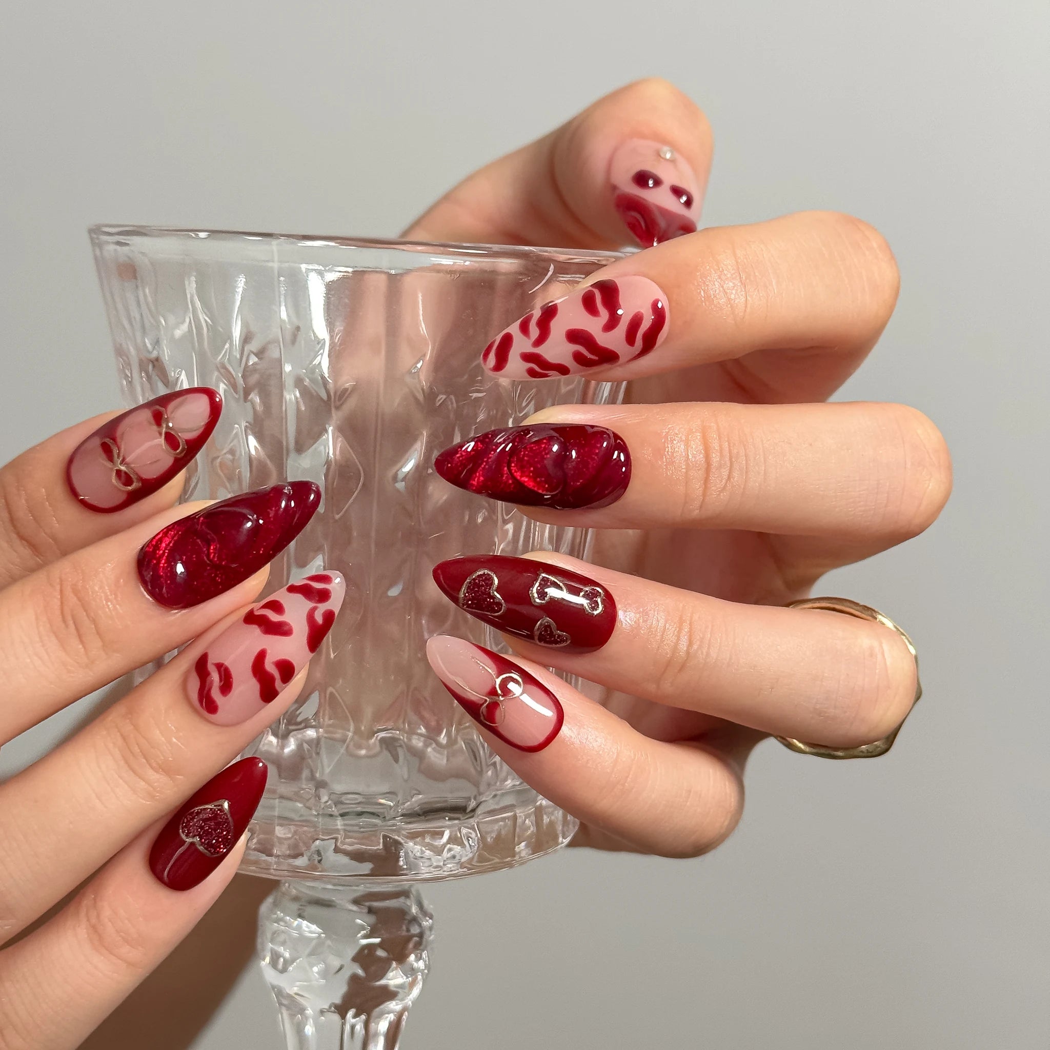 Aphrodite’s Stolen Kiss press-on nails holding a clear glass, showing red lip and bow details.