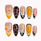 Vintage Havana Bloom: yellow, nude and brown almond press-on nails with spotted patterns, white flowers and starfish accents, set arranged on a pale background.