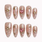 Gilded Heart Aura press-on nails in nude, pink, white, and gold with starburst accents, crystals, marble details, and a glitter heart