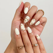 Pomona’s Azure Grove: cream press-on nails with pale blue stripes and tiny orange fruit motifs, shown on raised hands.
