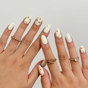 Pomona’s Azure Grove: cream press-on nails with pale blue stripes and tiny orange fruit motifs, shown on raised hands.