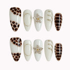 Bastet’s Desert Flower: white and brown almond press-on nails with spotted patterns, metallic outlines and star accents, set arranged on a pale background.